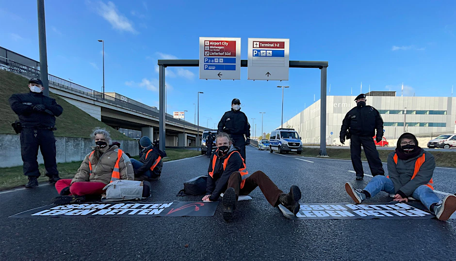 Aktivisten der Initiative "Aufstand der letzten Generation" blockieren eine Zufahrt zum Hauptstadt-Flughafen BER.