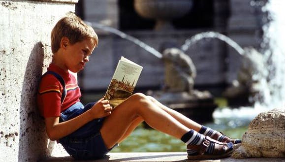 Versunken in einer anderen Welt: Ein Junge liest in einem Buch am Märchenbrunnen in Friedrichshain.
