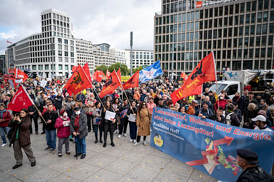 Teilnehmer stehen auf der Demonstration «Heizung, Brot & Frieden! Protestieren statt frieren» am Potsdamer Platz mit Fahnen und Plakaten.  