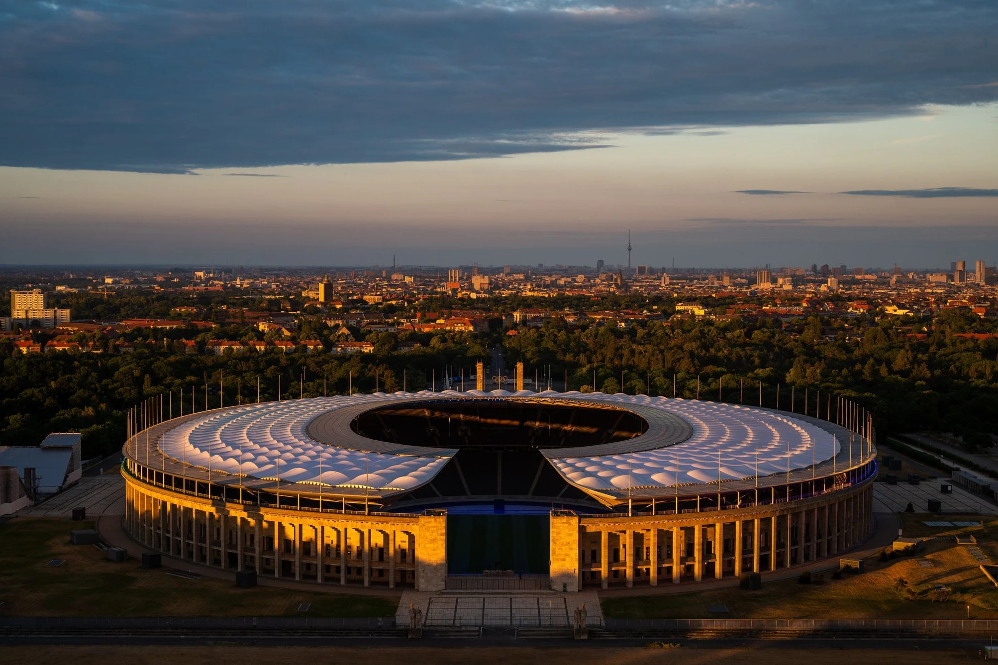 Die untergehende Sonne scheint auf das Olympiastadion. Im Hintergrund das Berliner Stadtzentrum.
