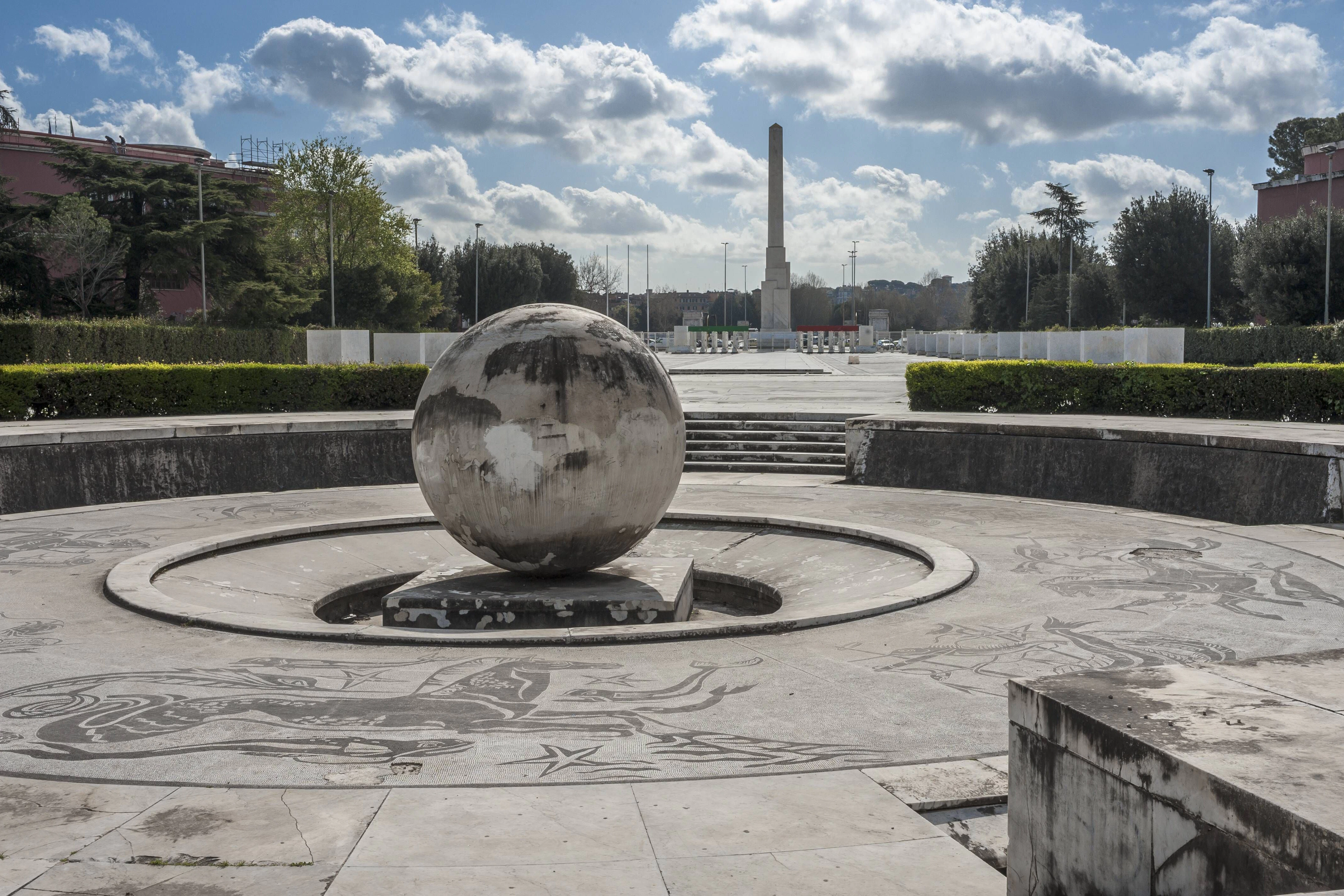 Im Vordergrund: Eine steinerne Weltkugel und Platz mit Marmor-Mosaiken. Im Hintergrund ist der Mussolini-Obelisk mit der lateinischen Inschrift "Mussolini Dux" zu sehen, daneben das Foro Italico, Sportstättenkomplex, erbaut zwischen 1928 und 1938, Rom, Italien.&nbsp;