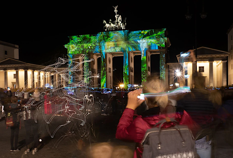 ARCHIV - Zahlreiche Menschen stehen 2020 beim "Festival of Lights" vor dem illuminierten Brandenburger Tor (Langzeitbelichtung).  