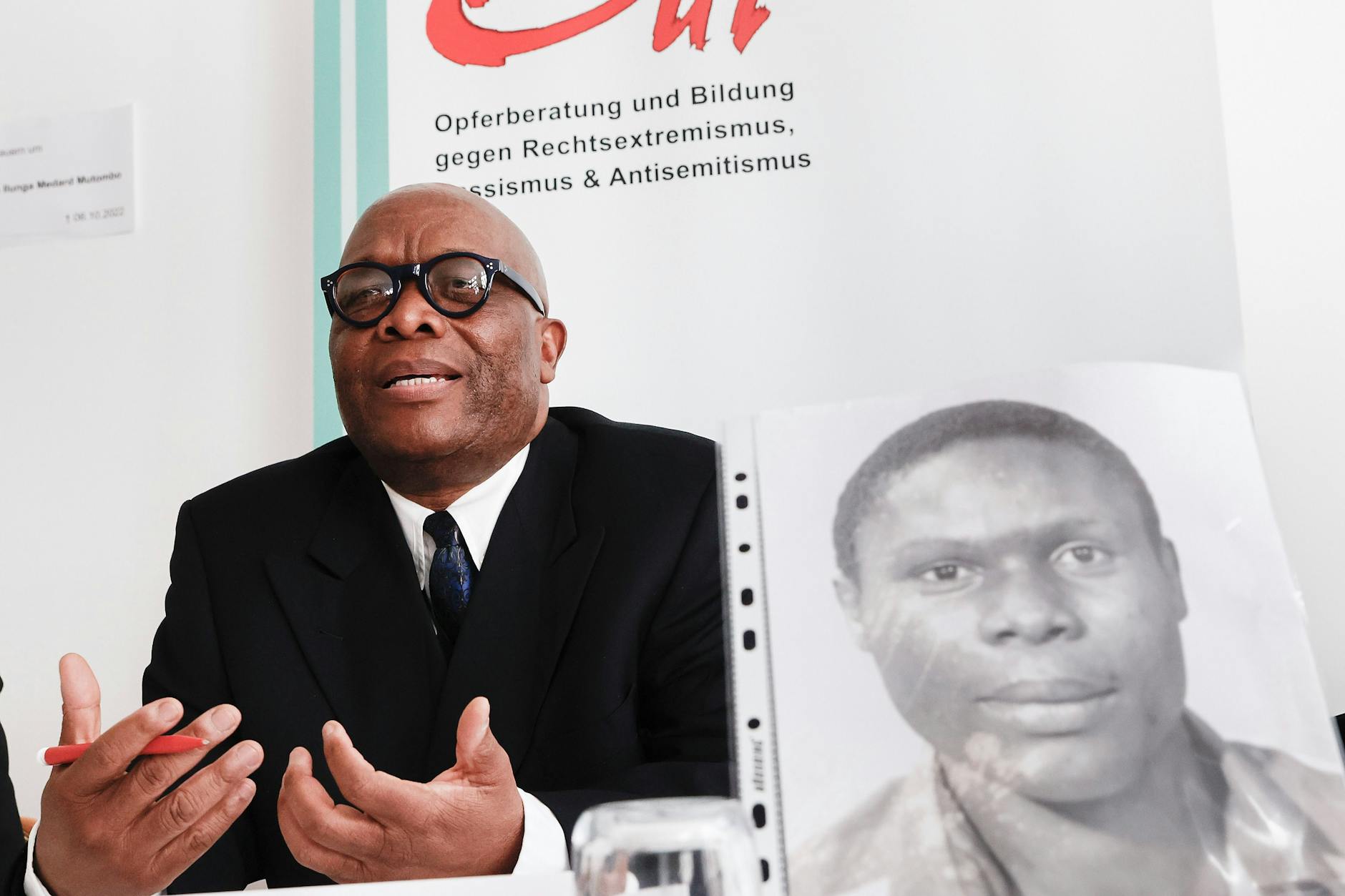 Warum musste Kupa Ilunga Medard Mutombo sterben? Mutombo Mansamba hat ein Foto seines Bruders zur Pressekonferenz mitgebracht.