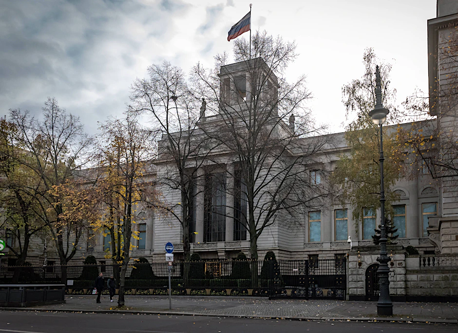 Die Flagge der russischen Botschaft weht am frühen Morgen vor einer roten Ampel in Berlin. Ändert sich bald ihre Adresse?