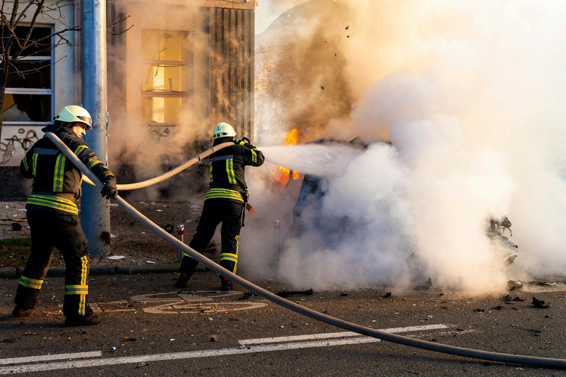 Einsatzkräfte der Feuerwehr versuchen, ein brennendes Auto nach einem Raketenangriff zu löschen. 