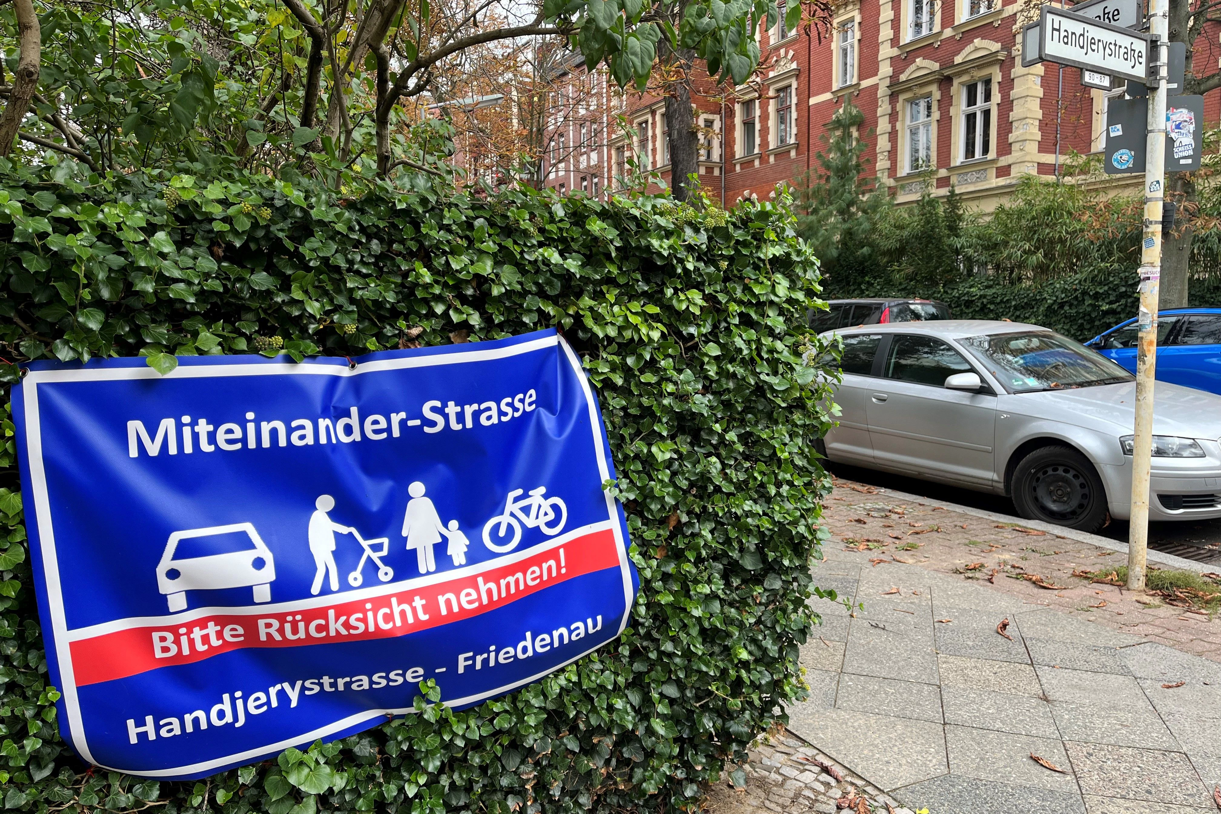 Ein Transparent an einem Vorgarten in der Handjerystraße. Bürger lehnen die Planung des Bezirks ab. Sie fordern eine Miteinander-Straße, in der alle gleichberechtigt sind. Derzeit ist das aber nicht der Fall – Autos dominieren.
