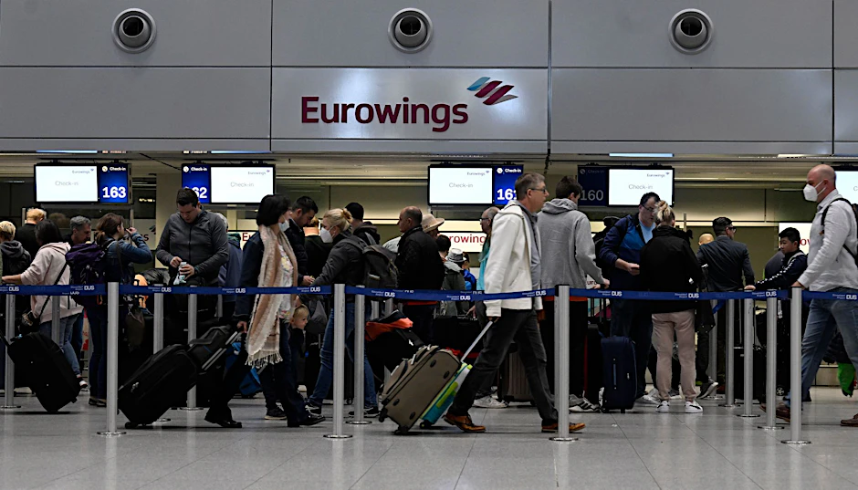 Reisende stehen am Eurowings Check-in-Schalter Schlange.