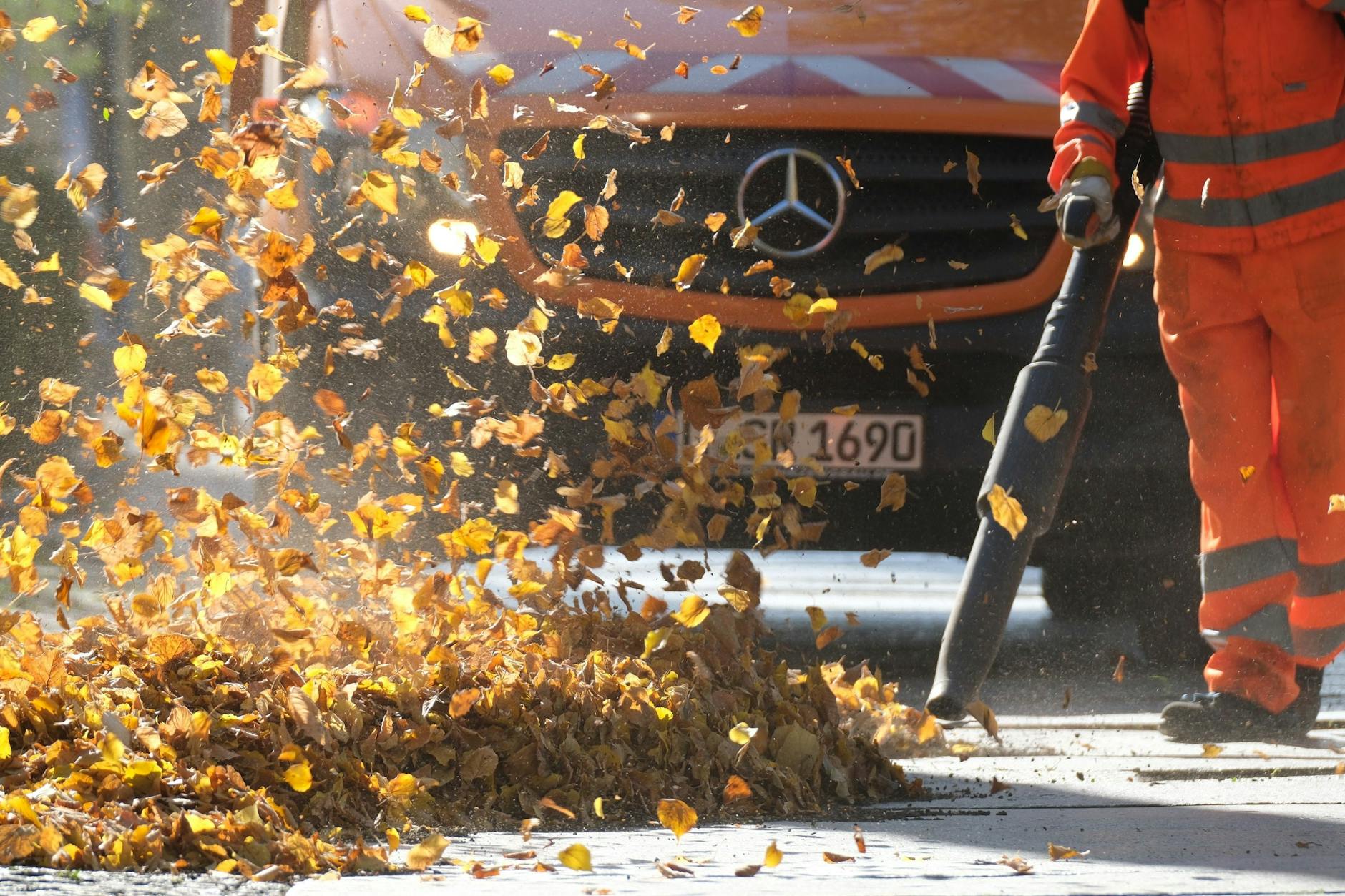 Ein Mitarbeiter der Stadtreinigung pustet Blätter mit einem Laubbläser weg.