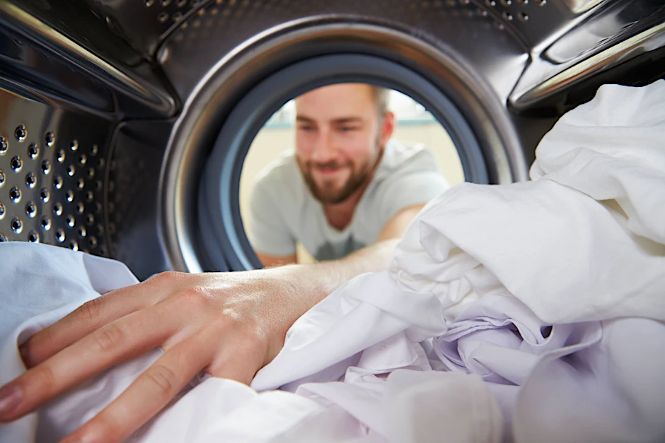 Mann räumt Wäsche in Waschmaschine.