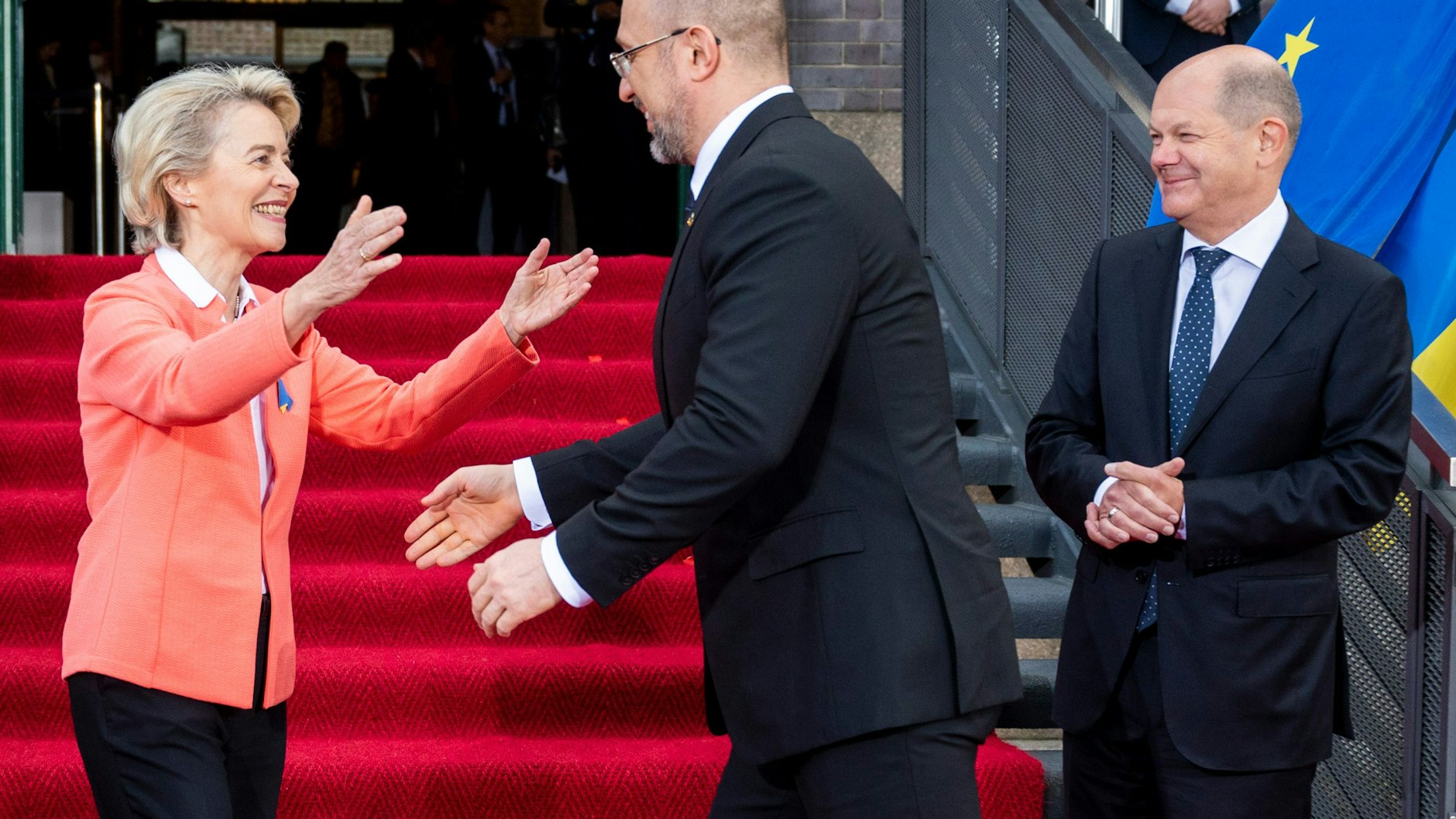 Bundeskanzler Olaf Scholz sieht verschmitzt zu, wie sich EU-Kommissionspräsidentin Ursula von der Leyen und der ukrainische Regierungschef Denys Schmyhal im Westhafen begrüßen.