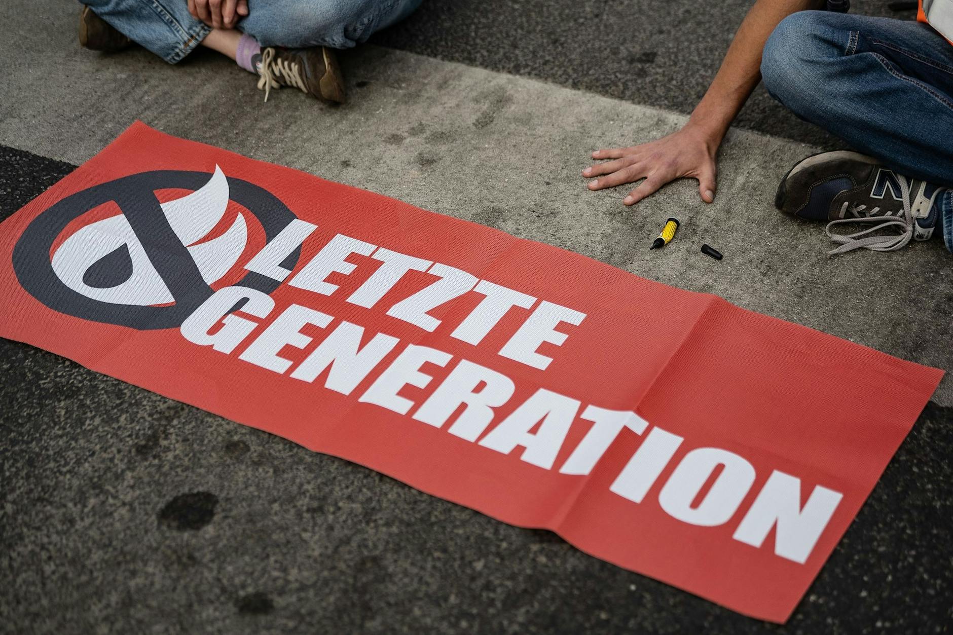 ARCHIV - Ein Aktivist der Gruppe "Letzte Generation", der seine Hand selbst auf der Straße festgeklebt hat, blockiert eine Kreuzung.