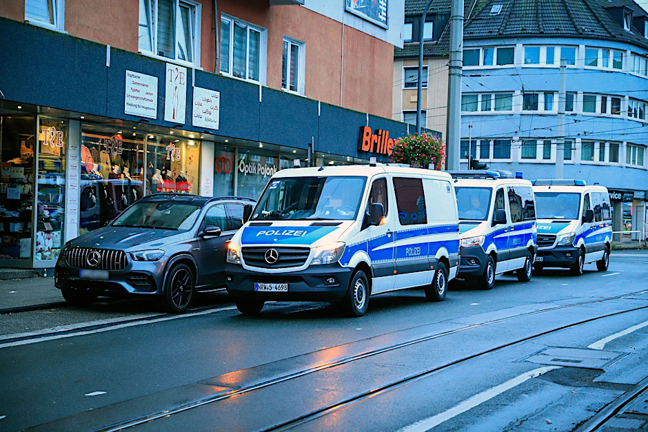 Fahrzeuge der Polizei stehen bei einer Razzia vor einem Hauseingang. (Archivbild)