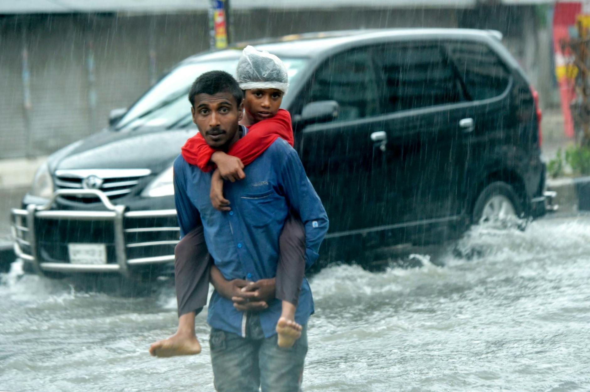 dpatopbilder - Ein Mann trägt in Dhaka einen Jungen auf dem Rücken, während er auf einer überschwemmten Straße geht.