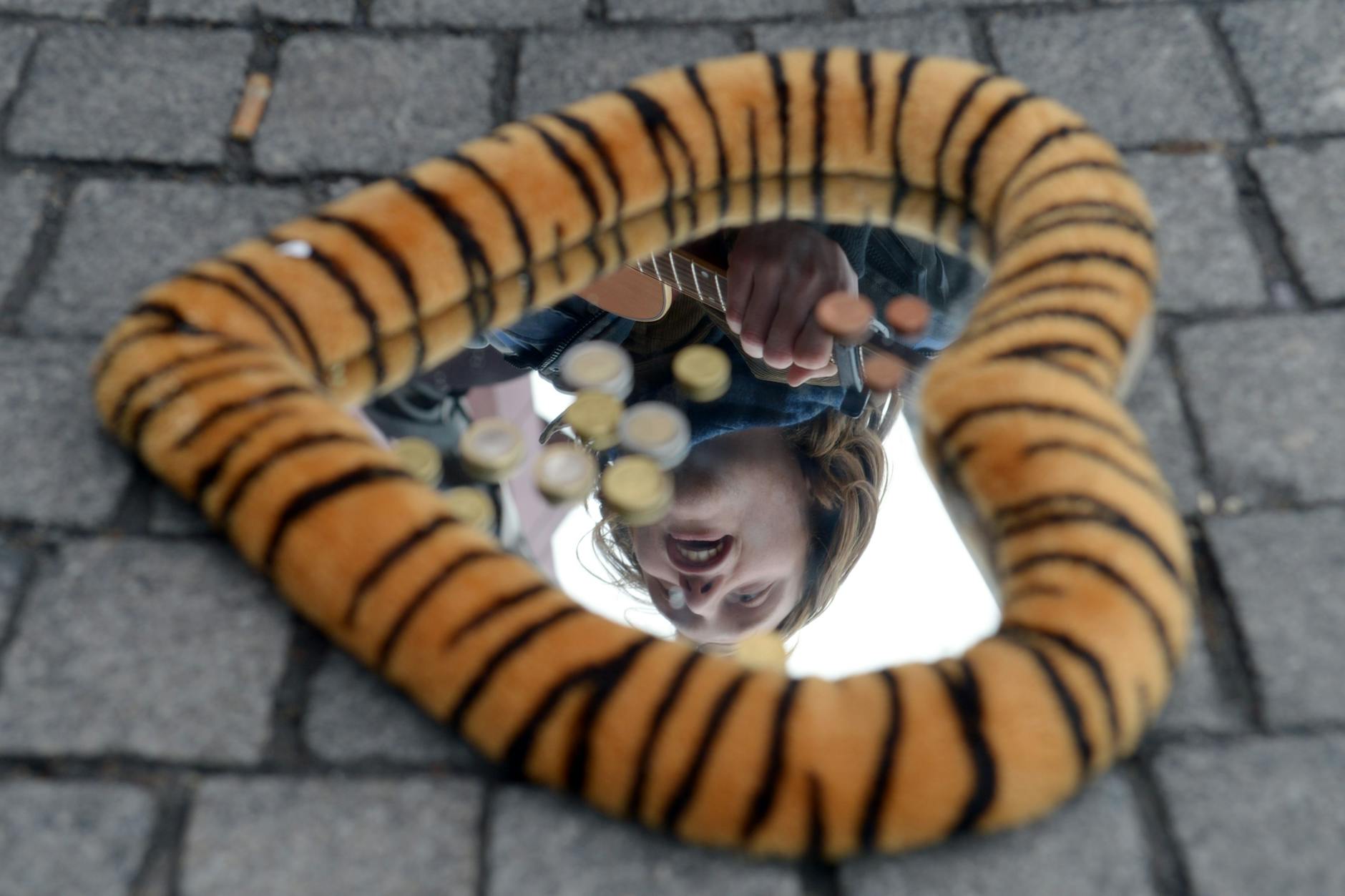 Ein Straßenmusiker spiegelt sich am Alexanderplatz in Berlin.