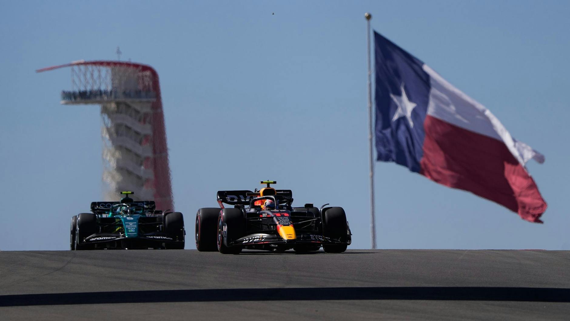 MotoRed-Bull-Pilot Sergio Perez (r) aus Mexiko, und Aston-Martin-Pilot Sebastian Vettel (l) aus Deutschland, steuern durch eine Kurve vor der Flagge von Texas.