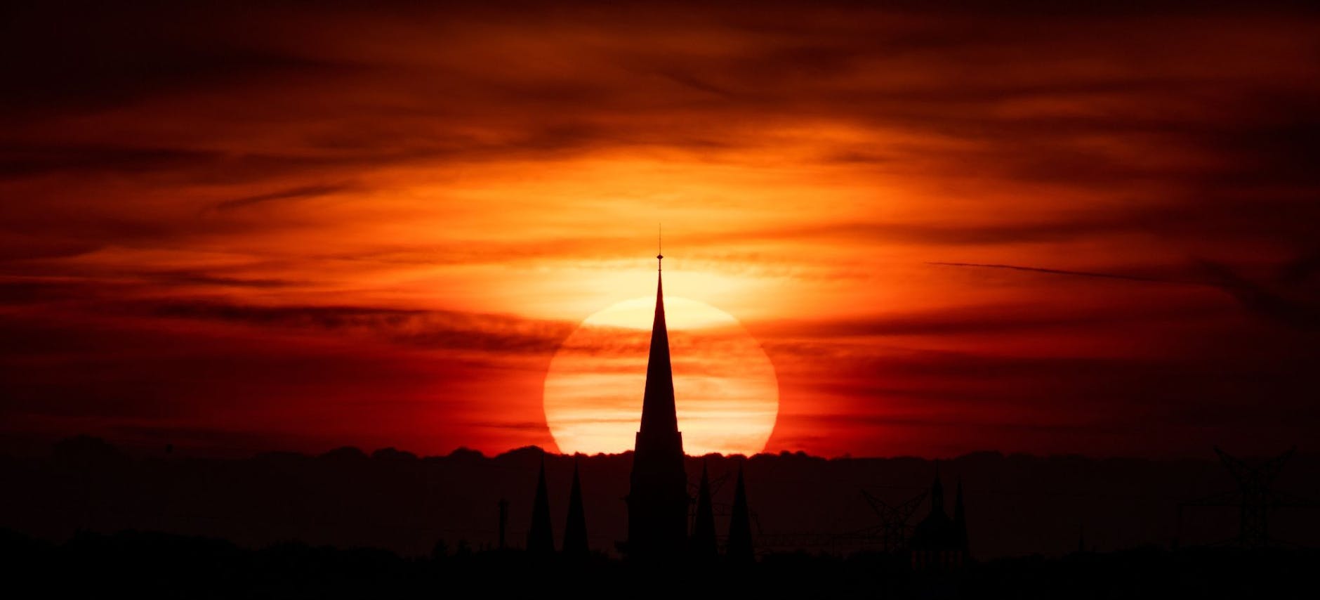 Die Sonne geht über der Oldenburger Lambertikirche unter und taucht die Stadt in ein warmes, rotes Licht.