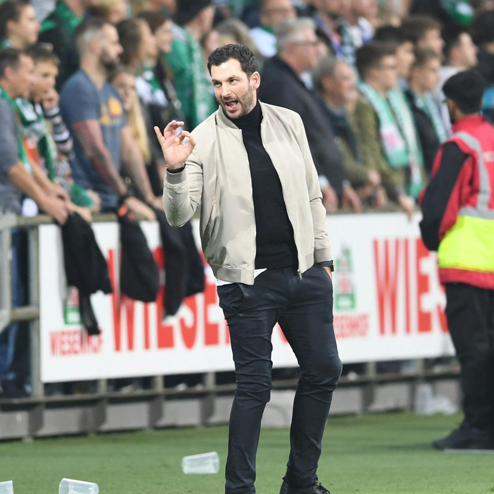 Leere Bierbecher liegen hinter Herthas Trainer Sandro Schwarz auf dem Rasen. 