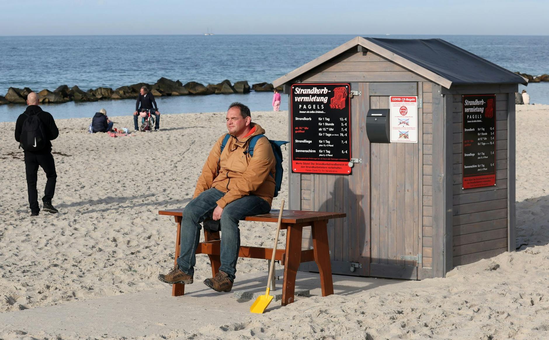 Ein Mann sitzt am Ostseestrand von Wustrow vor dem Häuschen eines Strandkorbvermieters und genießt das warme Wetter.