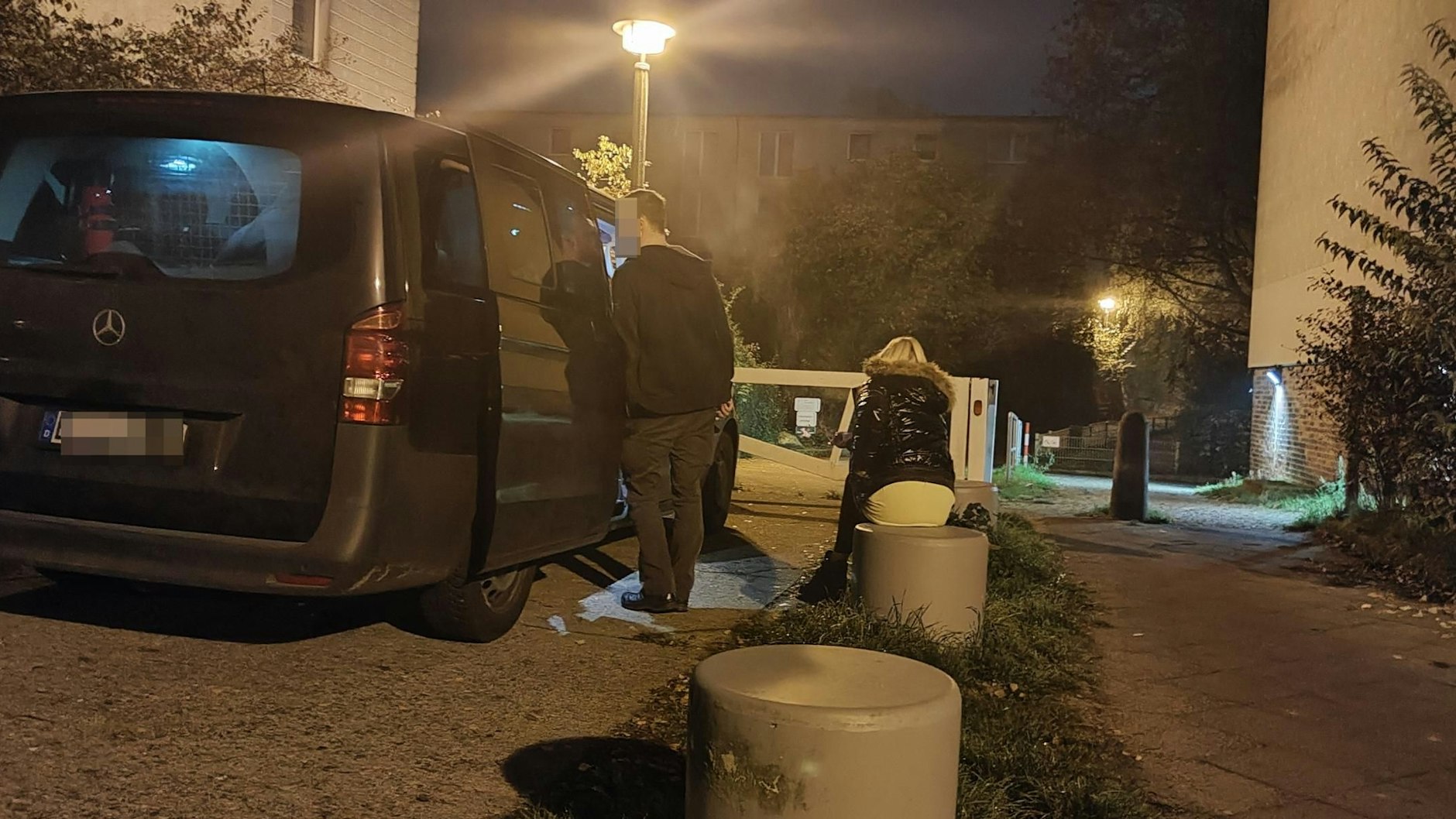Eine der beiden Frauen sitzt geschockt vor dem Haus auf einem Poller neben einem Polizeiauto