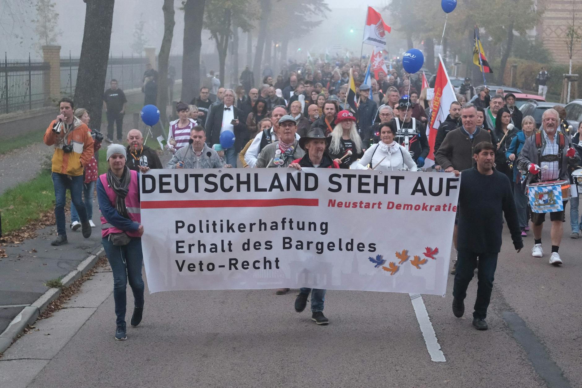 Lutherstadt Wittenberg: Teilnehmer einer Demonstration gehen mit einem Transparent und Fahnen eine Straße entlang. 