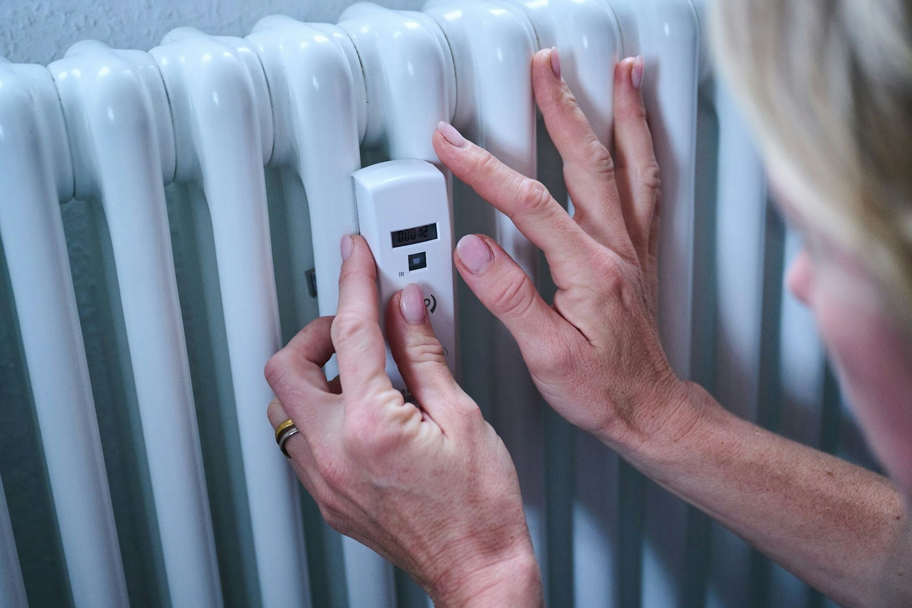Eine Frau kontrolliert einen Heizkostenverteiler an der Heizung.
