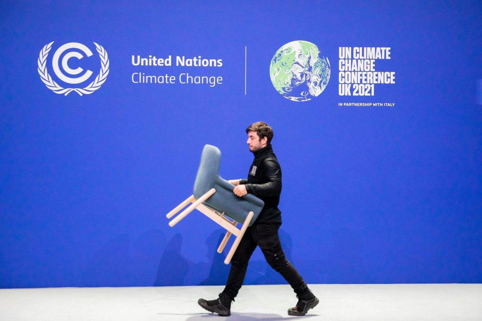 ARCHIV - Ein Mitarbeiter trägt bei der UN-Klimakonferenz COP26 einen Stuhl von einer Bühne.  