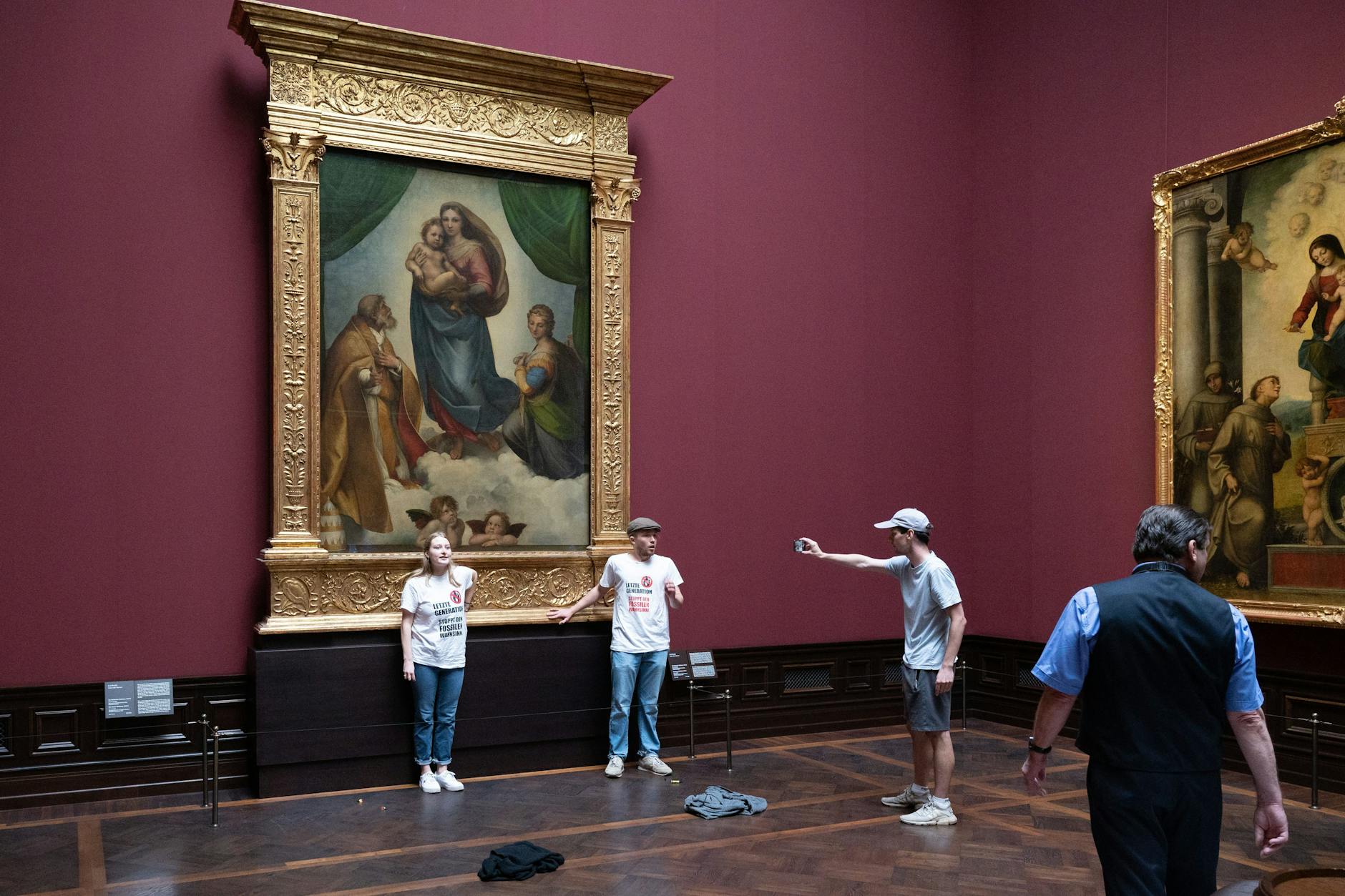 Zwei Umweltaktivisten der Gruppe „Letzte Generation“ stehen in der Gemäldegalerie Alte Meister in Dresden an dem Gemälde „Sixtinische Madonna“ von Raffael.