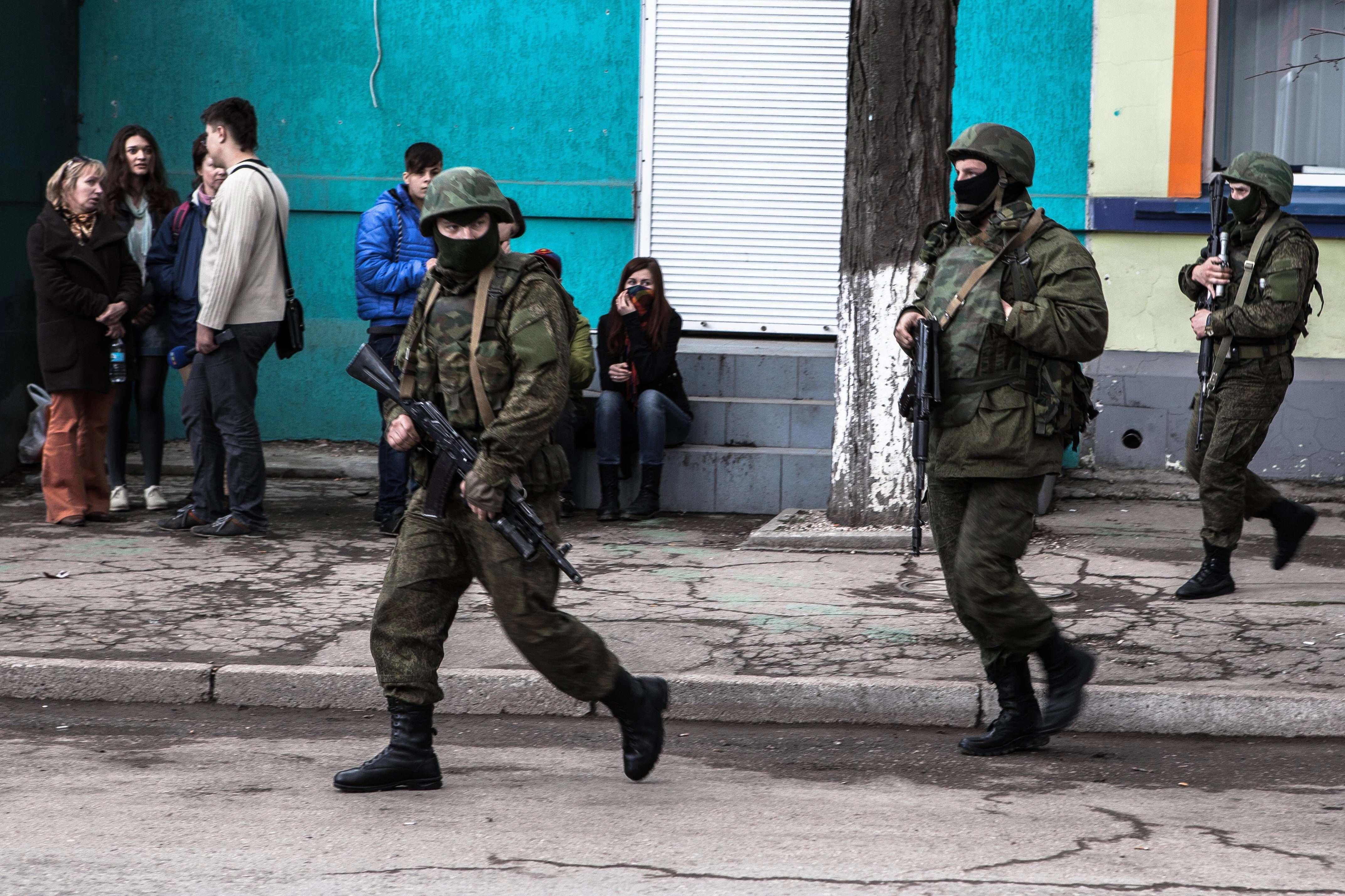 Mutmaßliche russische Soldaten mit Sturmgewehren und schweren Panzern laufen am 5. März 2014 über die Karl-Marx-Straße vor dem belagerten Hauptquartier der Küstenwache in Simferopol, Krim (Ukraine).