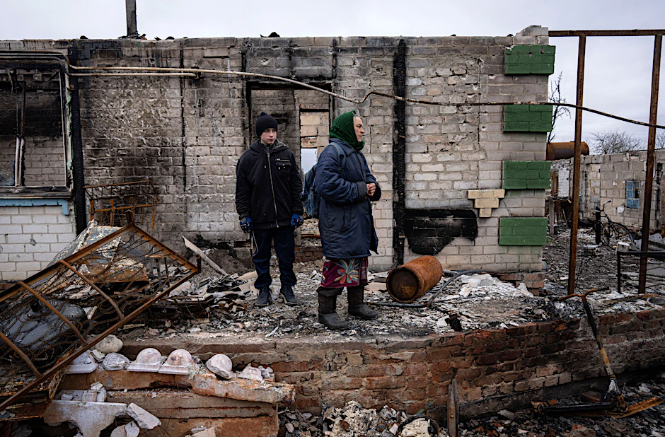 FILE - Danyk Rak, 12, stands with his grandmother Nina on the debris of their house destroyed by Russian forces