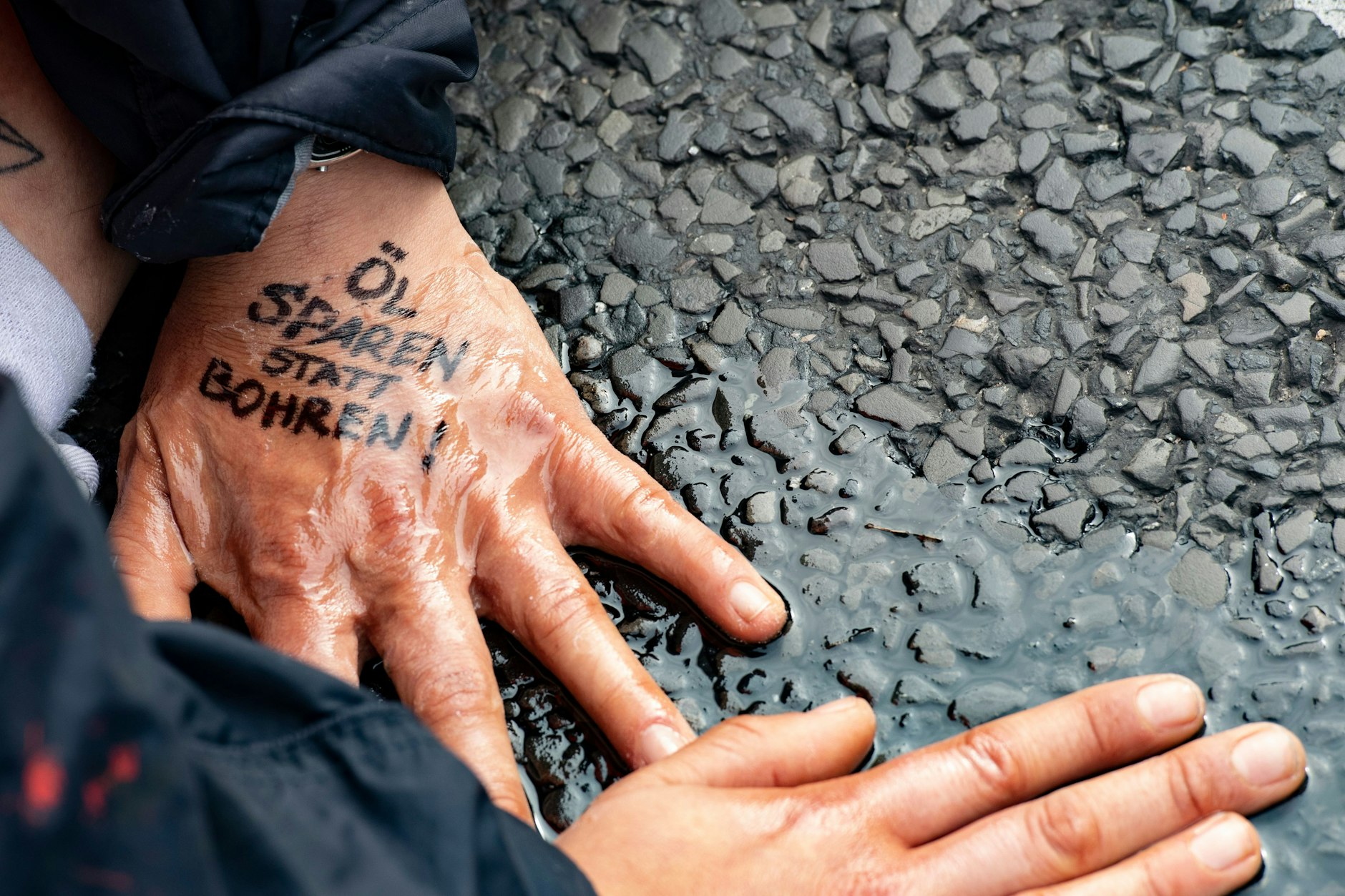 „Öl sparen statt bohren“ steht auf der Hand einer Demonstrantin der Gruppe „Letzte Generation“, die sich auf dem Asphalt festgeklebt hat.&nbsp;