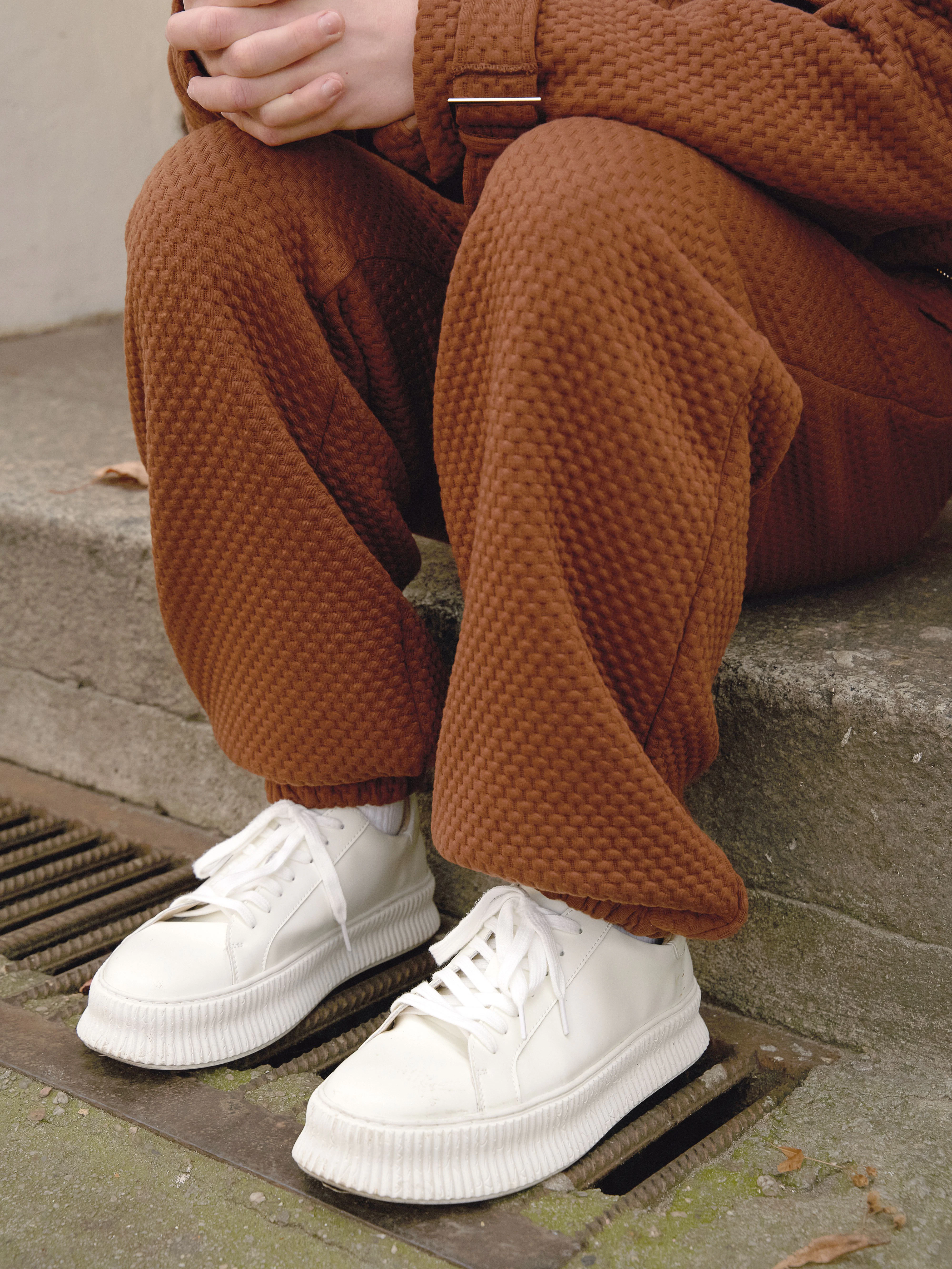 Zum braunen Anzug in Waffel-Optik trägt er schlohweiße Sneaker.