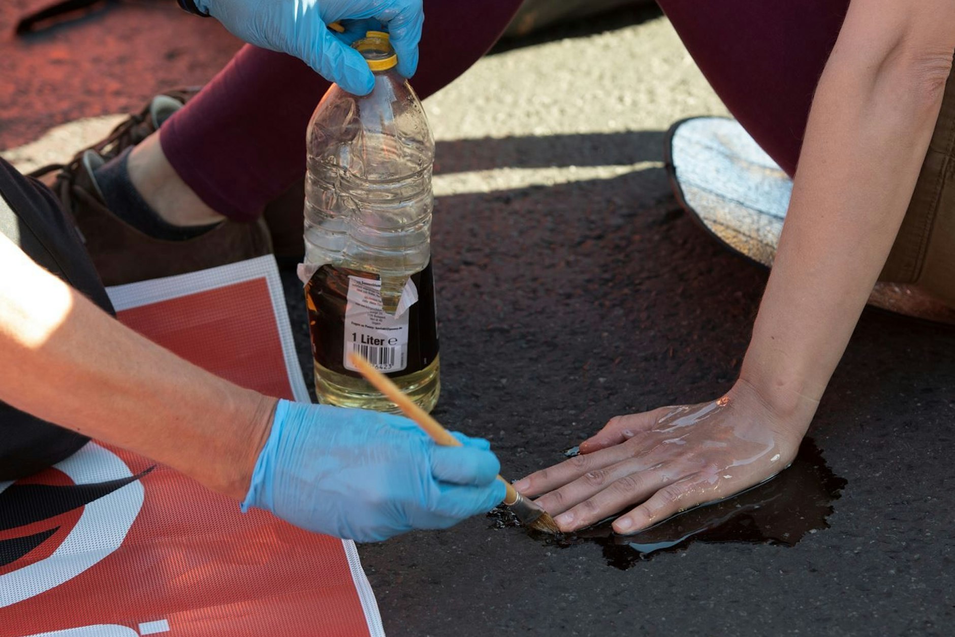 Berlin: Ein Polizeibeamter löst mit Sonnenblumenöl die festgeklebte Hand eines Klimaschutz-Demonstranten der Gruppe „Letzte Generation“ vom Asphalt. (Archivbild)