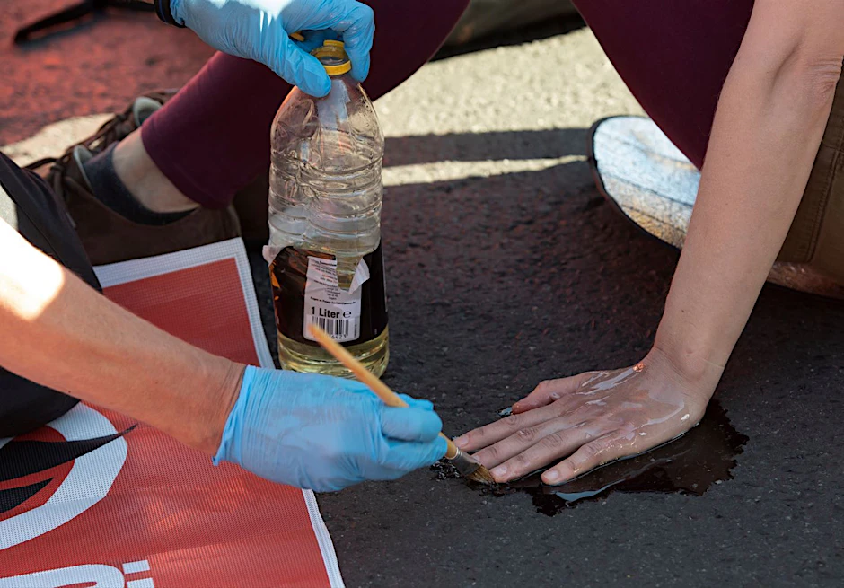 Berlin: Ein Polizeibeamter löst mit Sonnenblumenöl die festgeklebte Hand eines Klimaschutz-Demonstranten der Gruppe „Letzte Generation“ vom Asphalt. (Archivbild)