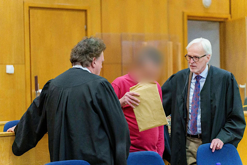 Der Angeklagte steht zwischen seinen Anwälten.  