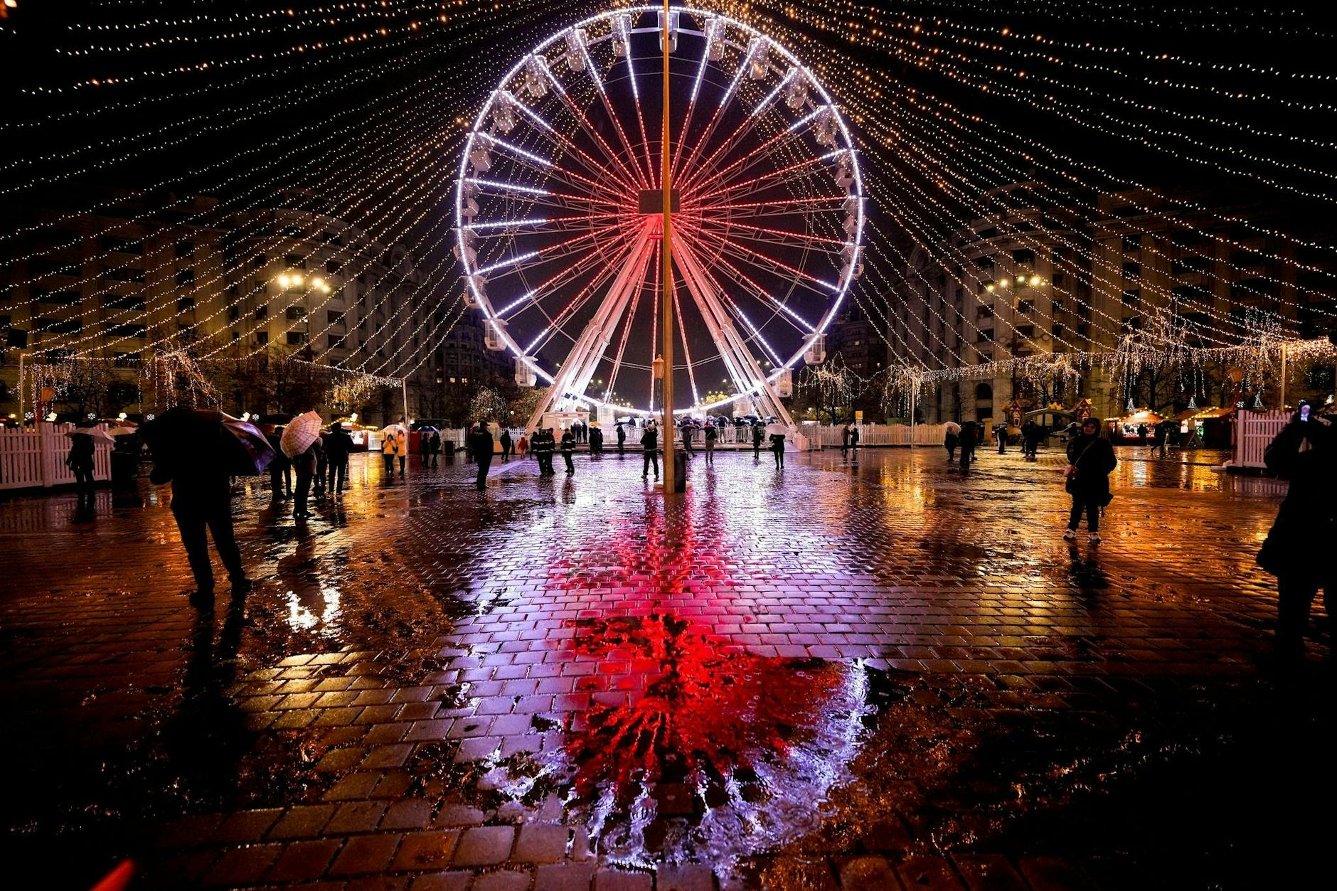 Ein beleuchtetes Riesenrad spiegelt sich auf dem nassen Bürgersteig eines Weihnachtsmarktes in der rumänischen Hauptstadt Bukarest.