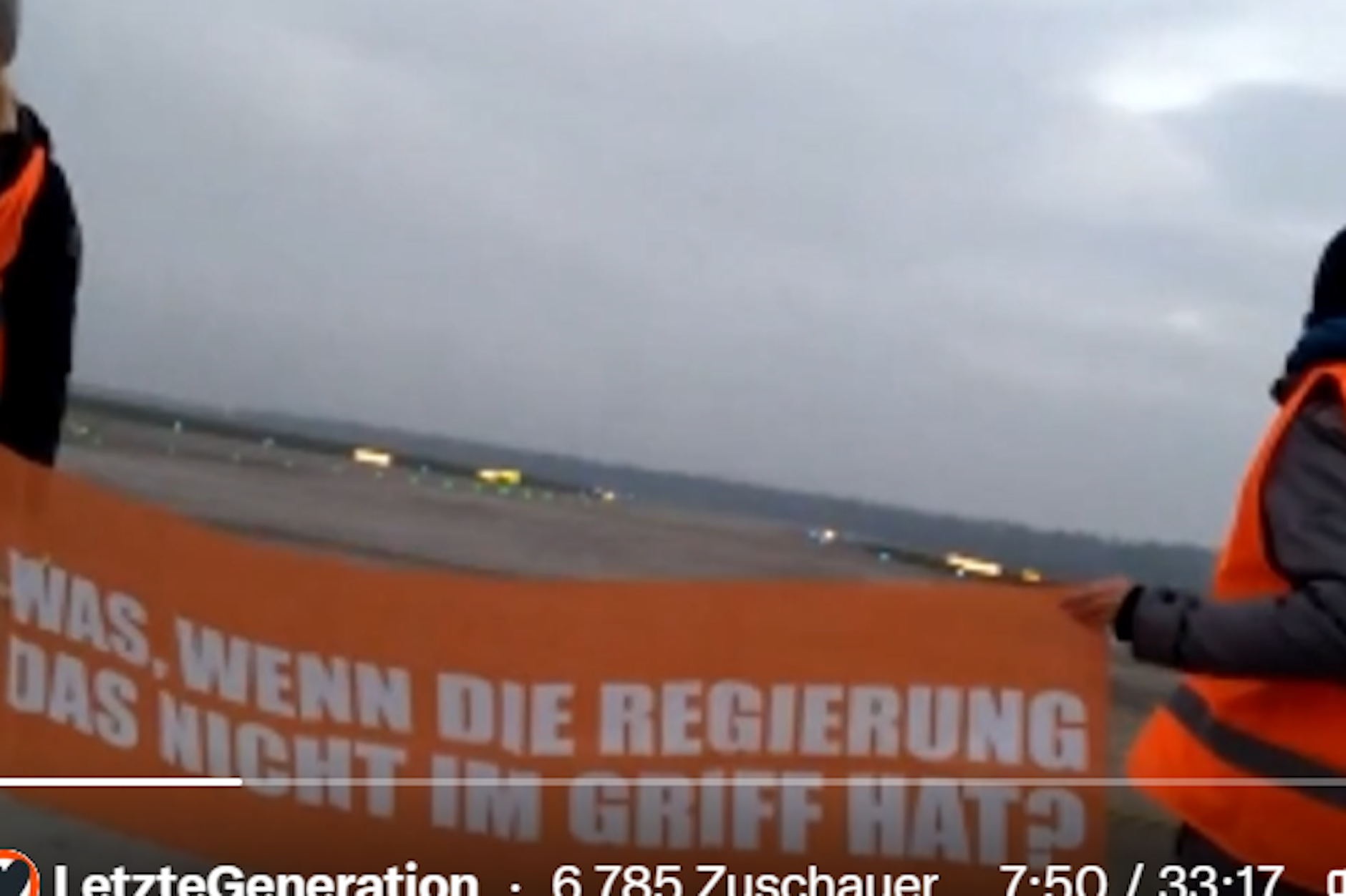 Im Livestream zu sehen: Klima-Kleber der Letzten Generation haben sich mit einem Transparent auf einem BER-Rollfeld postiert.