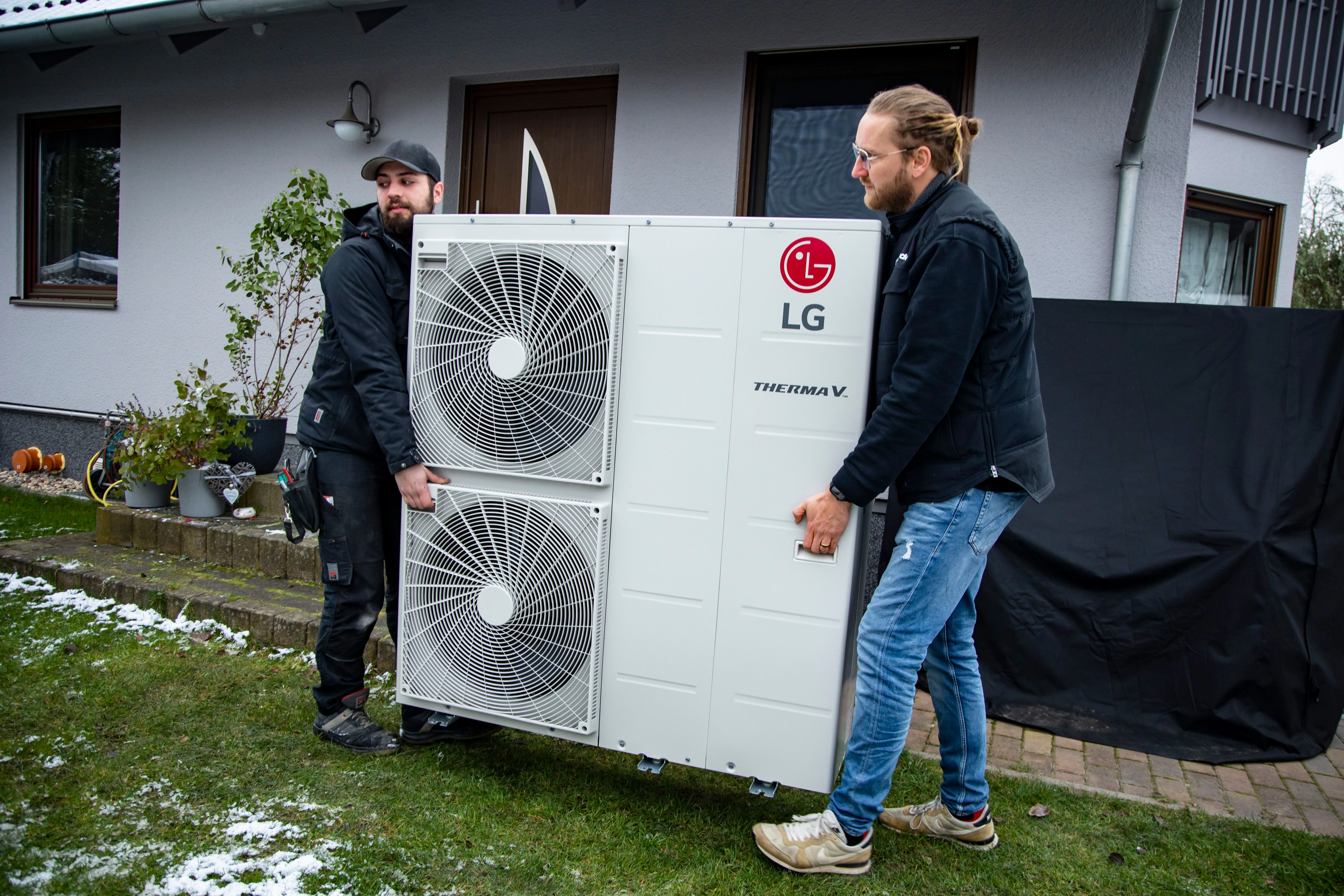 Die Wärmepumpe ist da: Monteur Daniele Russo und Gebietsleiter Christian Beggerow tragen das Gerät zum Fundament, auf das es montiert wird.