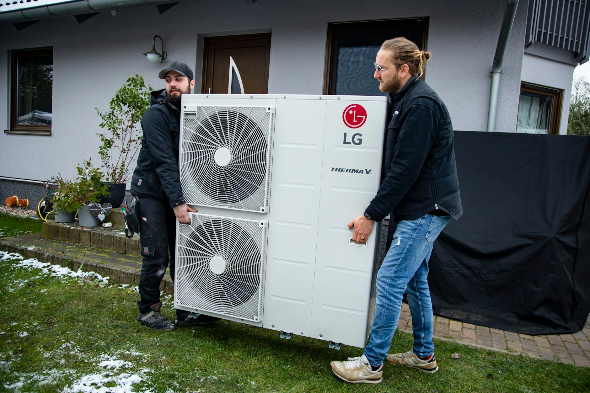 Die Wärmepumpe ist da: Monteur Daniele Russo und Gebietsleiter Christian Beggerow tragen das Gerät zum Fundament, auf das es montiert wird.