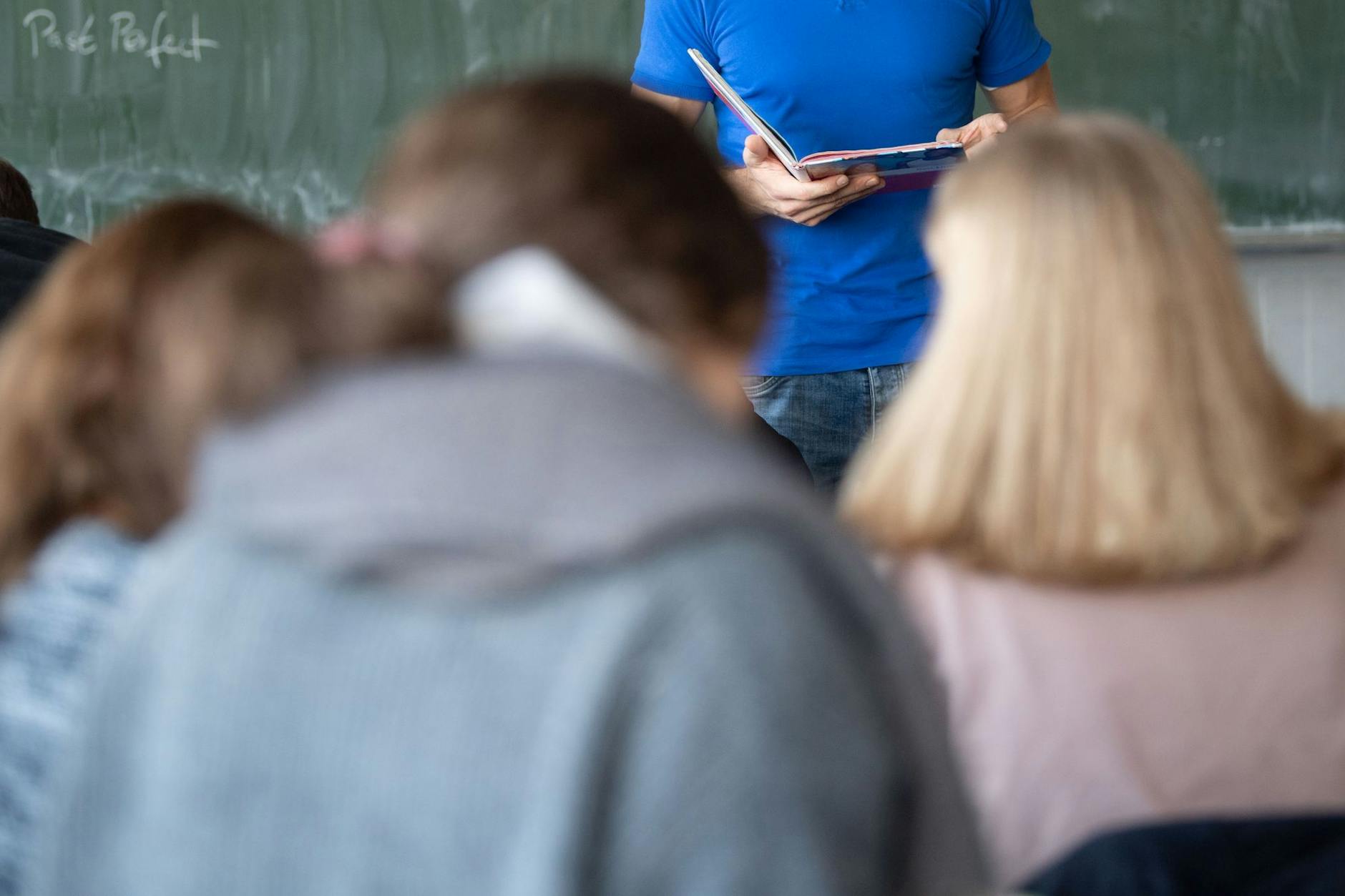 Ein Lehrer steht im Unterricht an der Tafel. Berliner Lehrkräfte, die nicht verbeamtet sind, sollen 300 Euro Ausgleich erhalten.