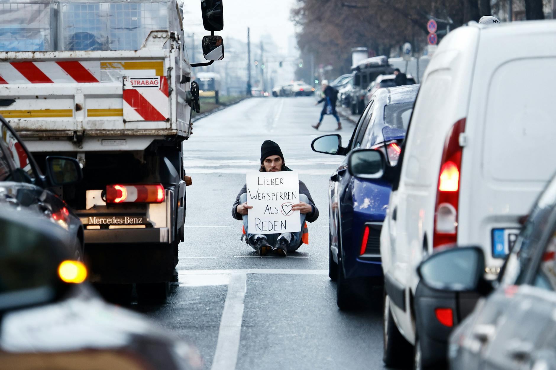 Ein Aktivist zeigt ein Schild mit der Aufschrift „Lieber Wegsperren als Reden“ bei einer Sitzblockade mit weiteren Aktivisten auf der Prenzlauer Allee.