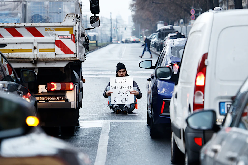Ein Aktivist zeigt ein Schild mit der Aufschrift „Lieber Wegsperren als Reden“ bei einer Sitzblockade mit weiteren Aktivisten auf der Prenzlauer Allee. 