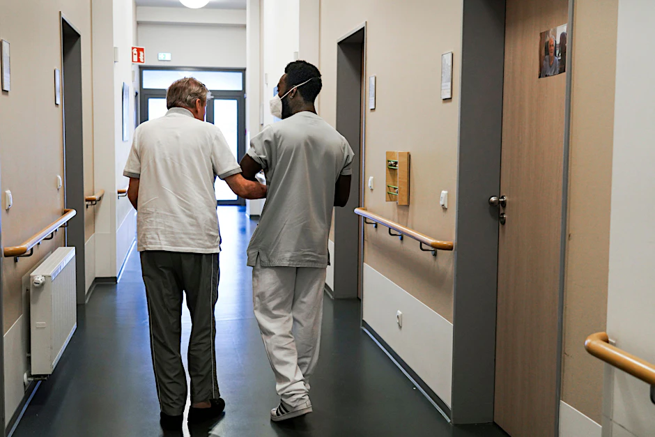 Ein Pfleger führt einen Heimbewohner über einen Gang: Viele Pflegekräfte fallen in diesem Jahr erkrankt aus.