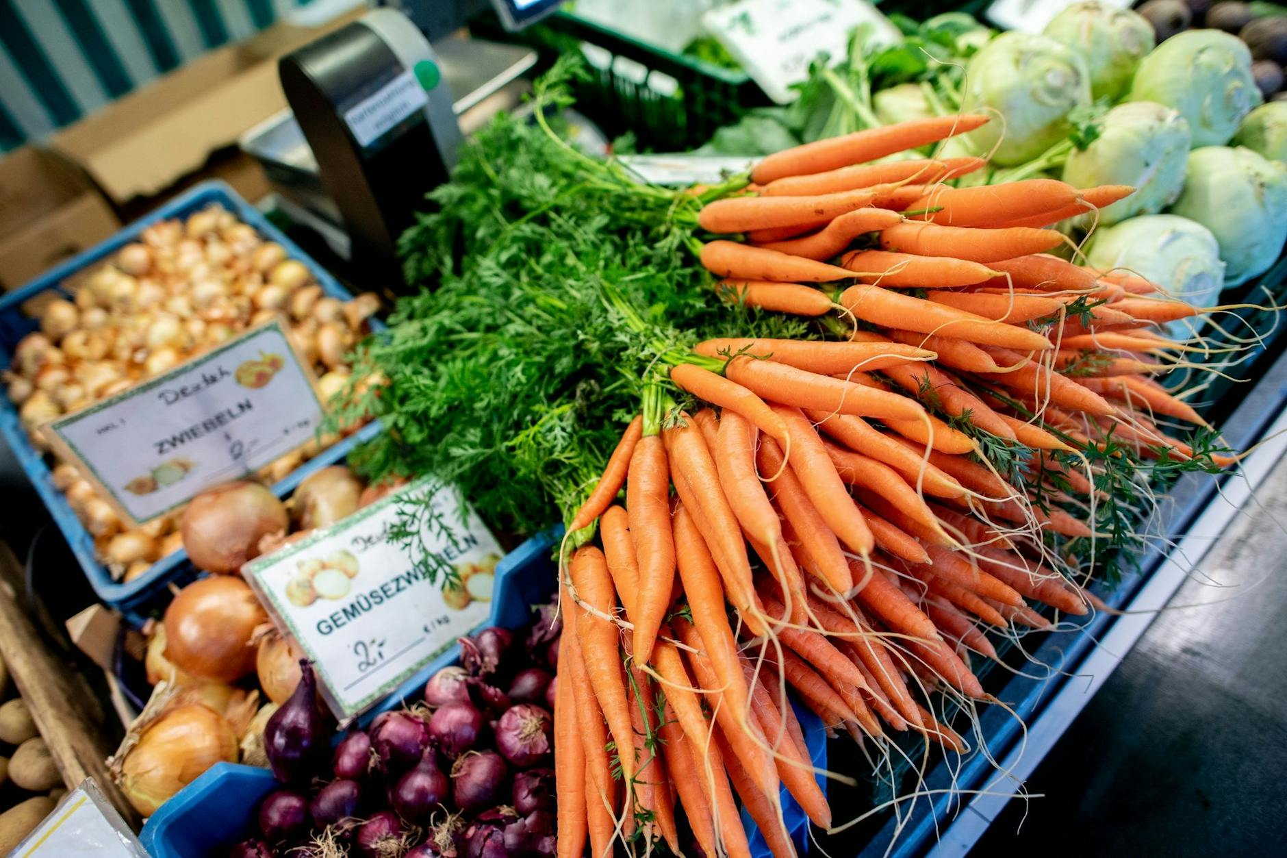 ARCHIV - Karotten und Zwiebeln stehen an einem Obst- und Gemüsestand auf einem Wochenmarkt zum Verkauf.