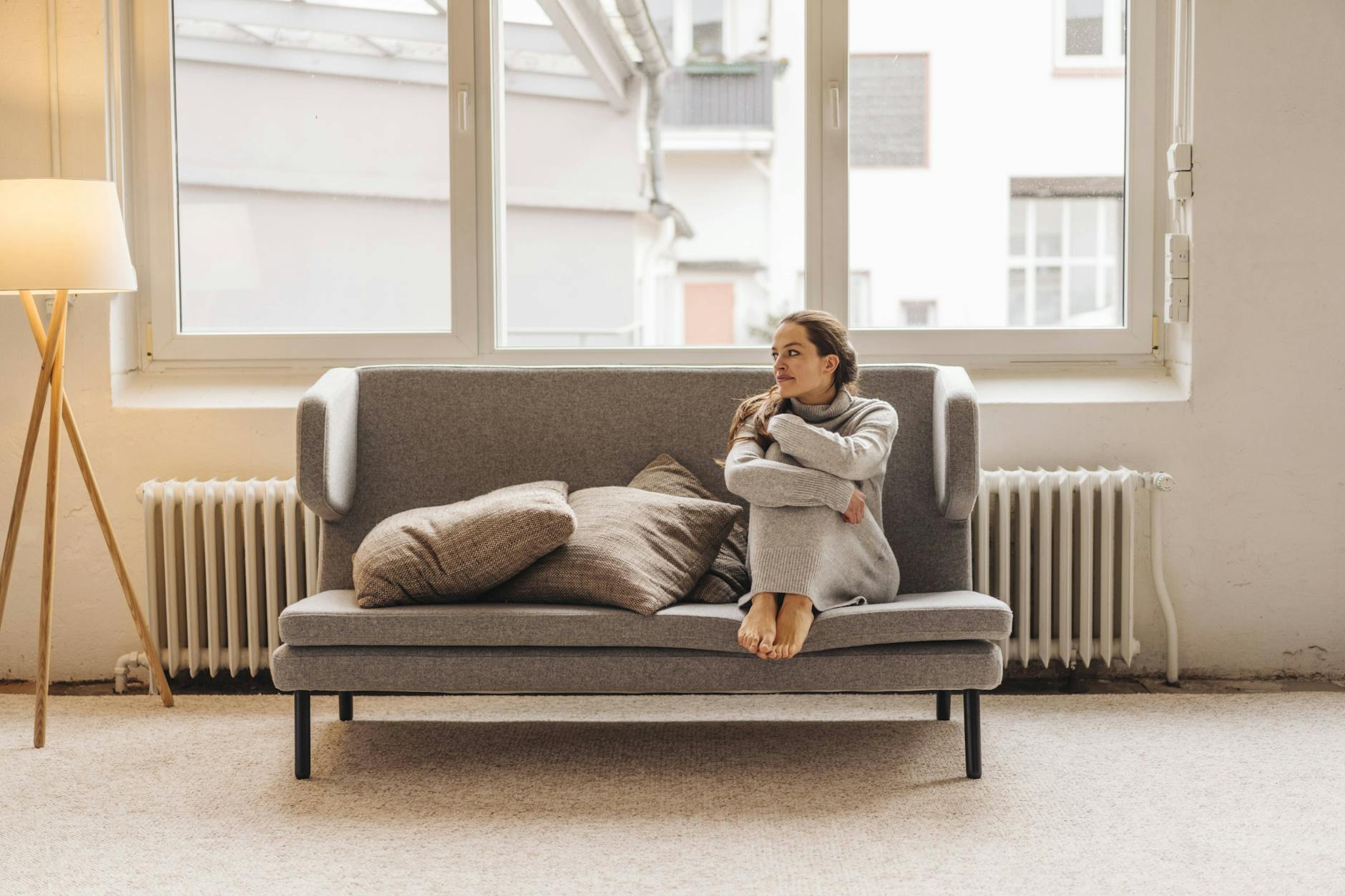 Eine junge Frau wärmt sich auf dem Sofa vor der Heizung.