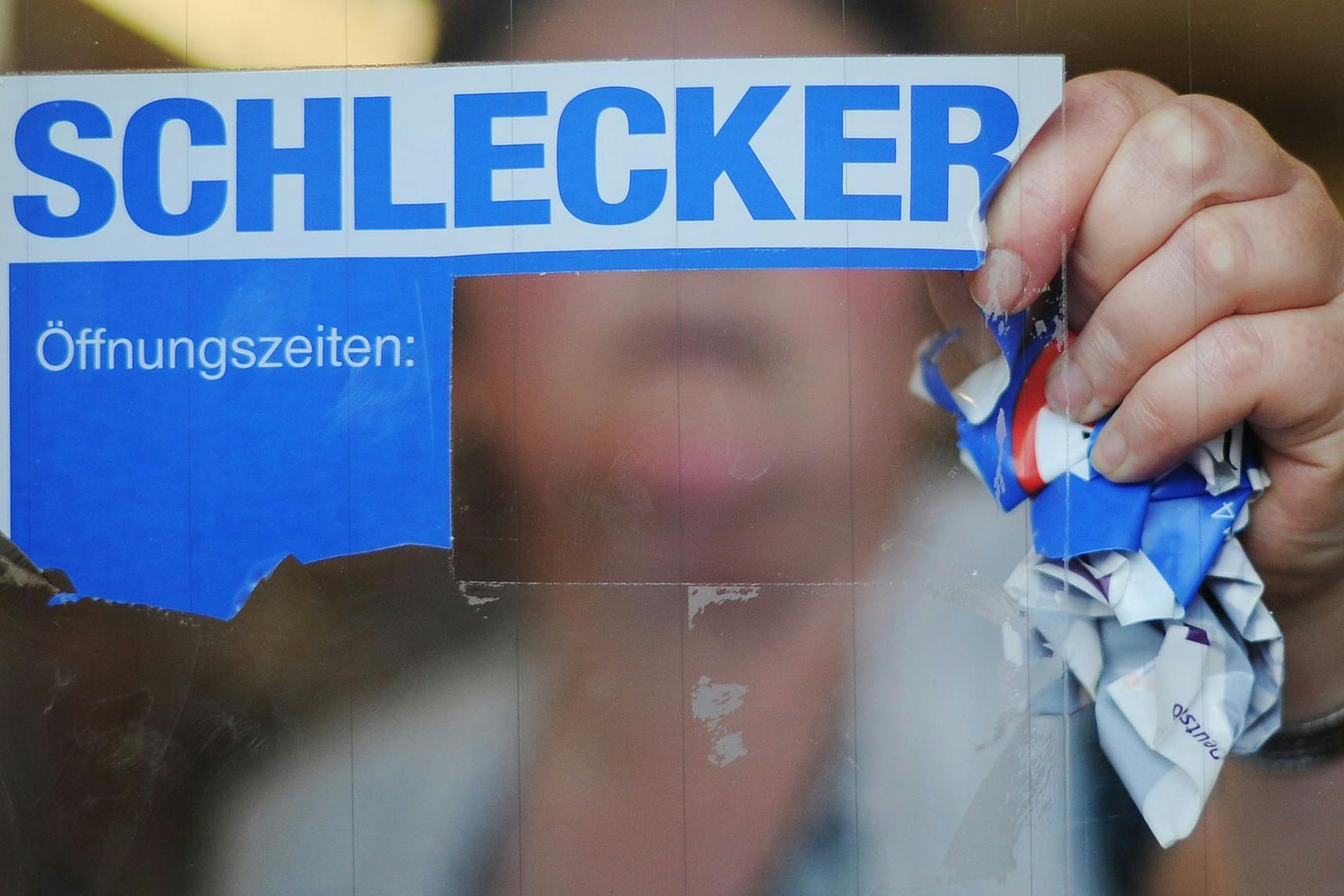 Die Schlecker-Pleite 2012: Eine Mitarbeiterin der Drogeriemarktkette reißt das Firmenlogo von der Eingangstür einer Filiale. Bis heute warten tausende Beschäftigte auf ihr Geld.