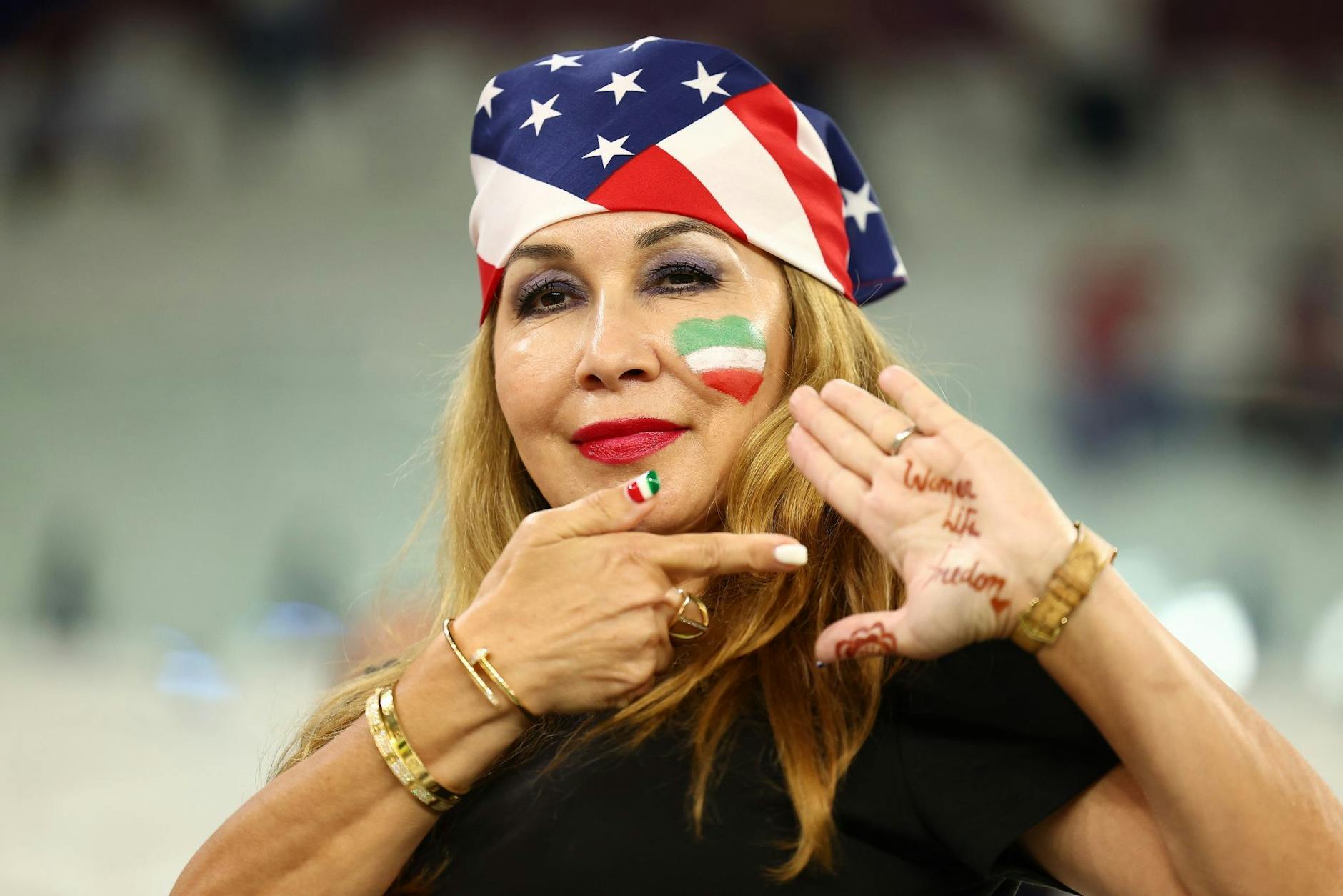 Ein Fan mit einer Kopfbedeckung in amerikanischen Landesfarben zeigt "Woman Life Freedom" auf ihrer Handfläche.