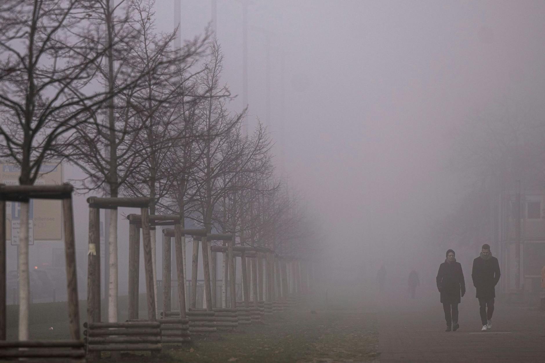 Passanten gehen am Morgen über einen vernebelten Gehweg in Berlin. Die Wetteraussichten sind trüb und kalt. 