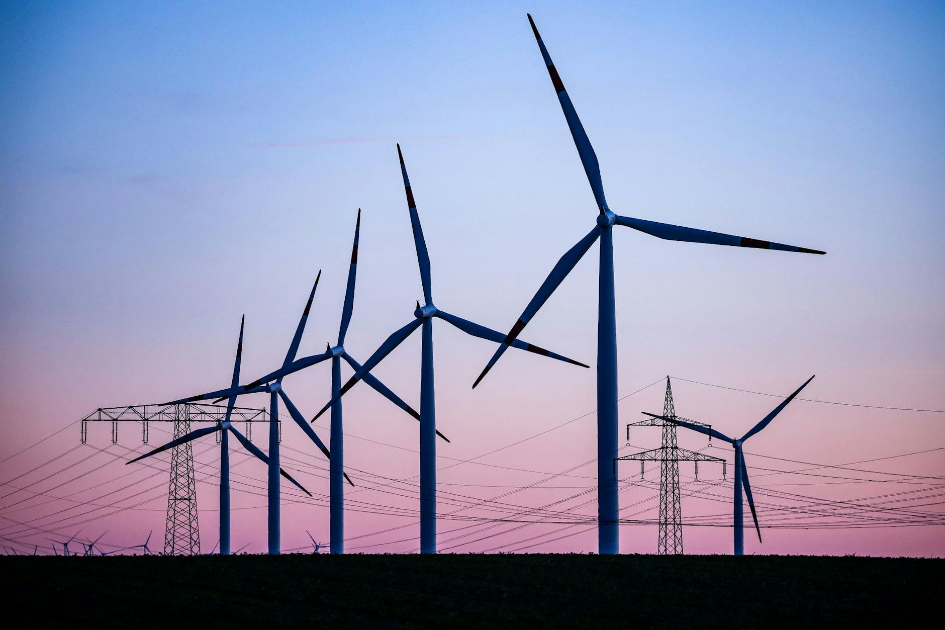 ARCHIV - Windkraftanlagen und Hochspannungsleitungen sind vor dem Abendhimmel bei Leuna zu sehen.