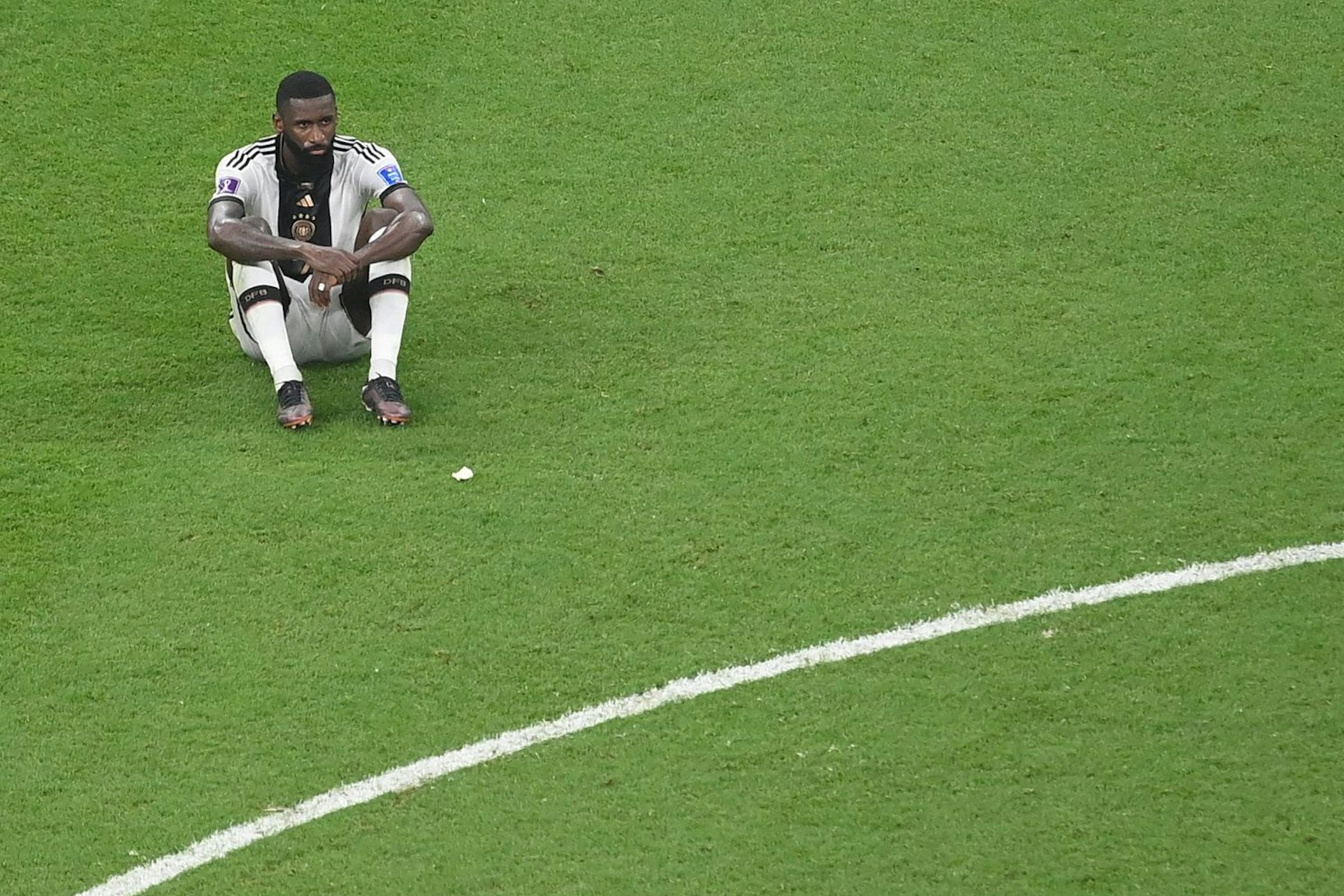 Antonio Rüdiger sitzt verloren auf dem Rasen im Al-Bayt-Stadium.