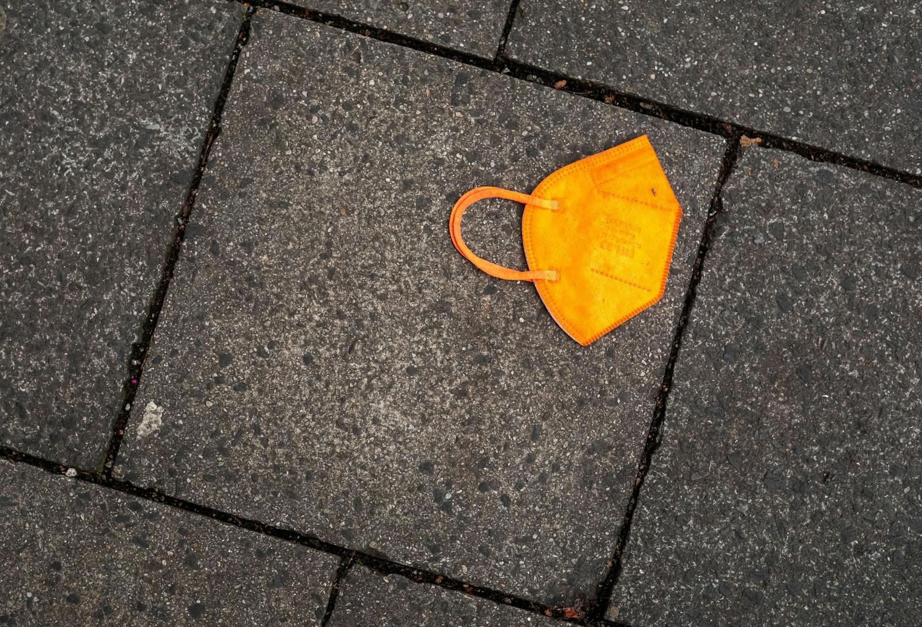 ARCHIV - Ein gebrauchter orangefarbener Mund-Nasen-Schutz liegt auf dem Gehweg.